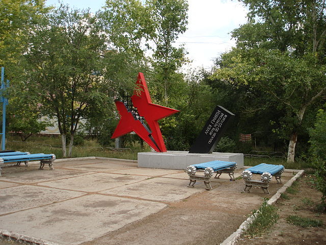A small concrete square with four blue benches and a statue of a large red star split down the middle by a lightning bolt. 