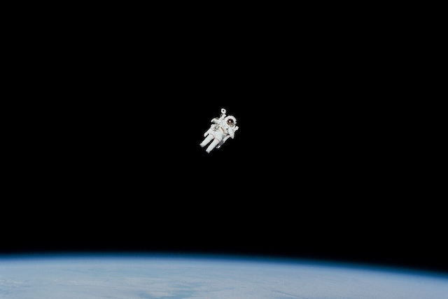 An astronaut floating in pitch-black space above the earth.