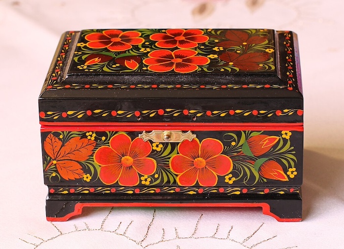A black wooden box ornately painted with red flowers and green leaves. 