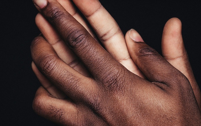 Two Black hands embrace in front of a black background.